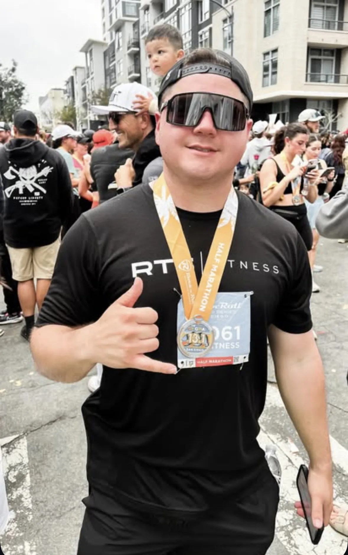 Coach Ray at a half marathon finish, wearing his medal and giving a thumbs up.