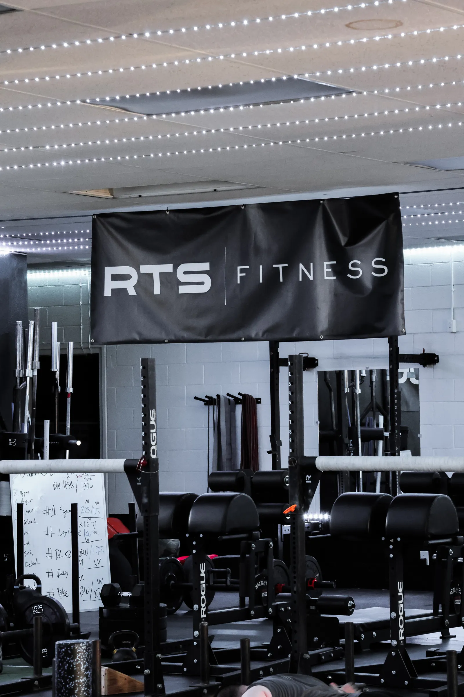Inside RTS Fitness: Rogue racks, barbells, a whiteboard and the RTS banner.
